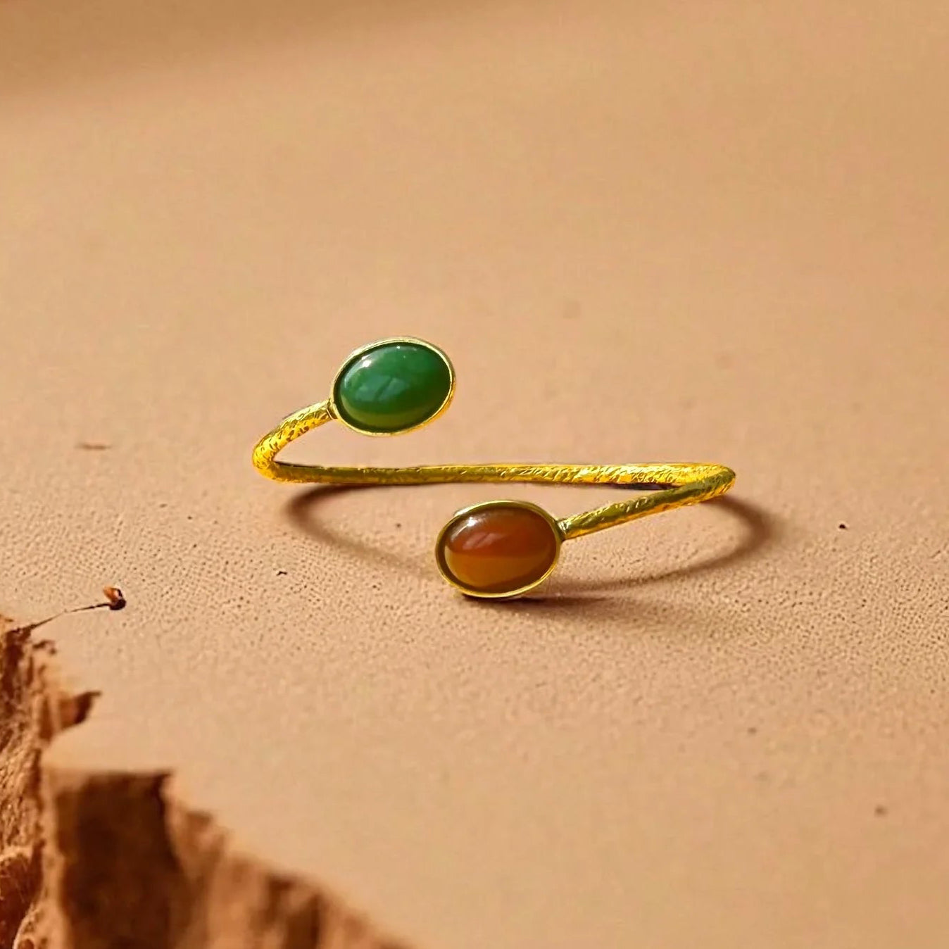 Gold ring with two colored stones on a sandy surface