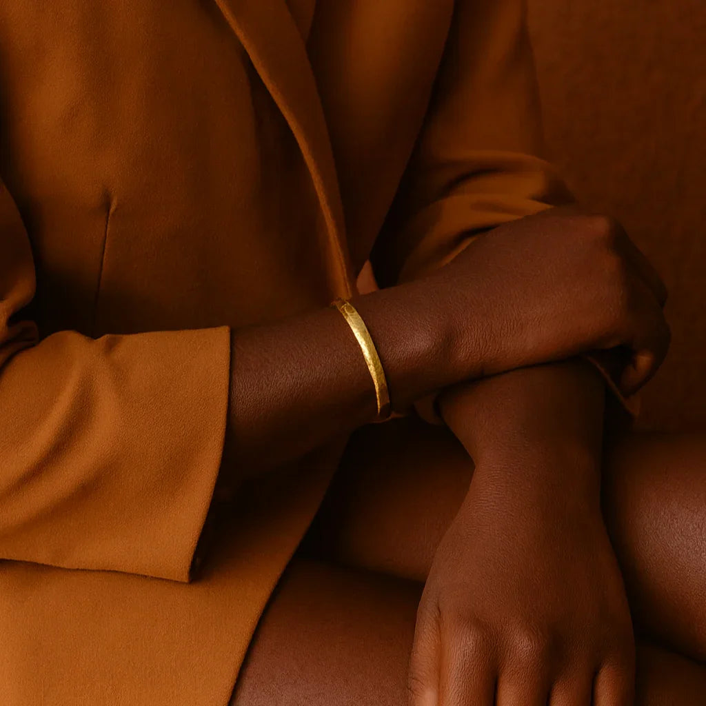 Person wearing a brown coat with a gold bracelet on a brown background