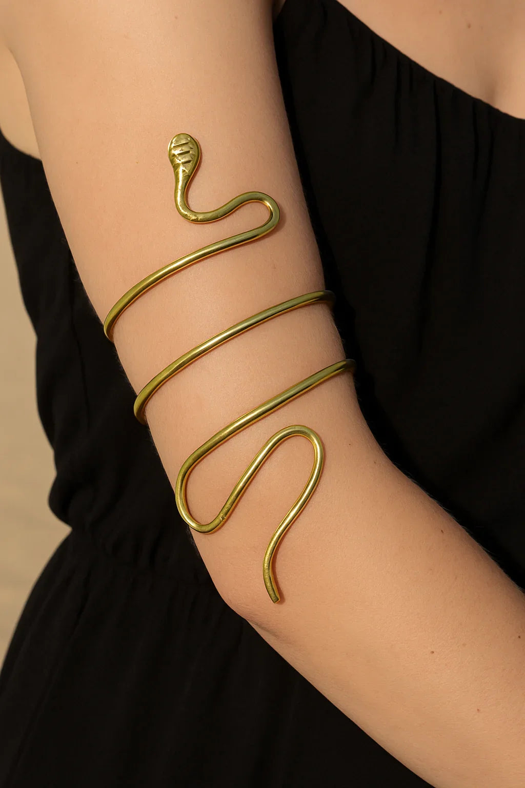Gold snake-shaped bracelet on a person's wrist against a black background