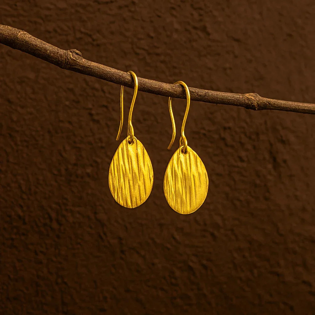 Gold earrings hanging on a branch against a brown background