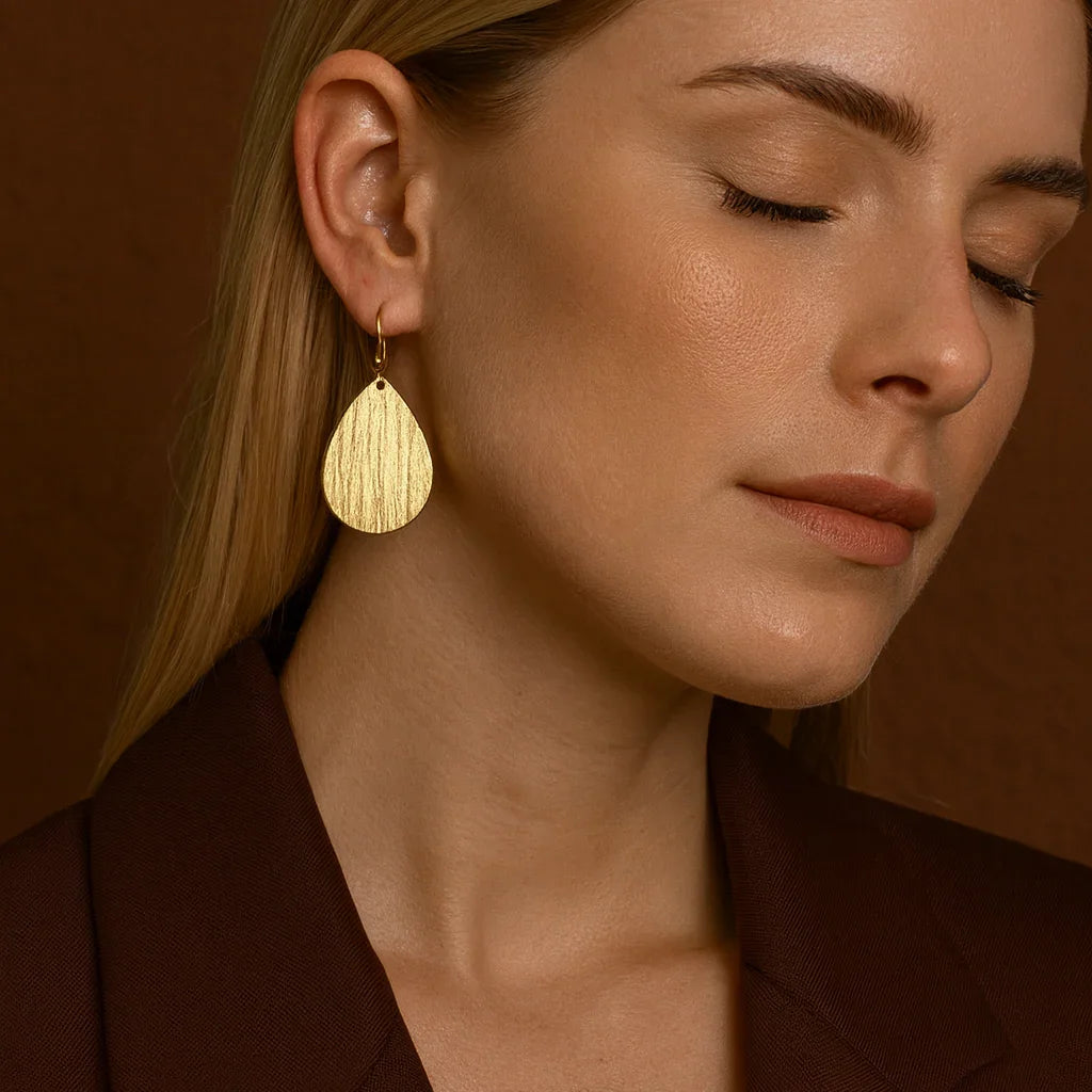 Woman wearing gold earrings against a brown background