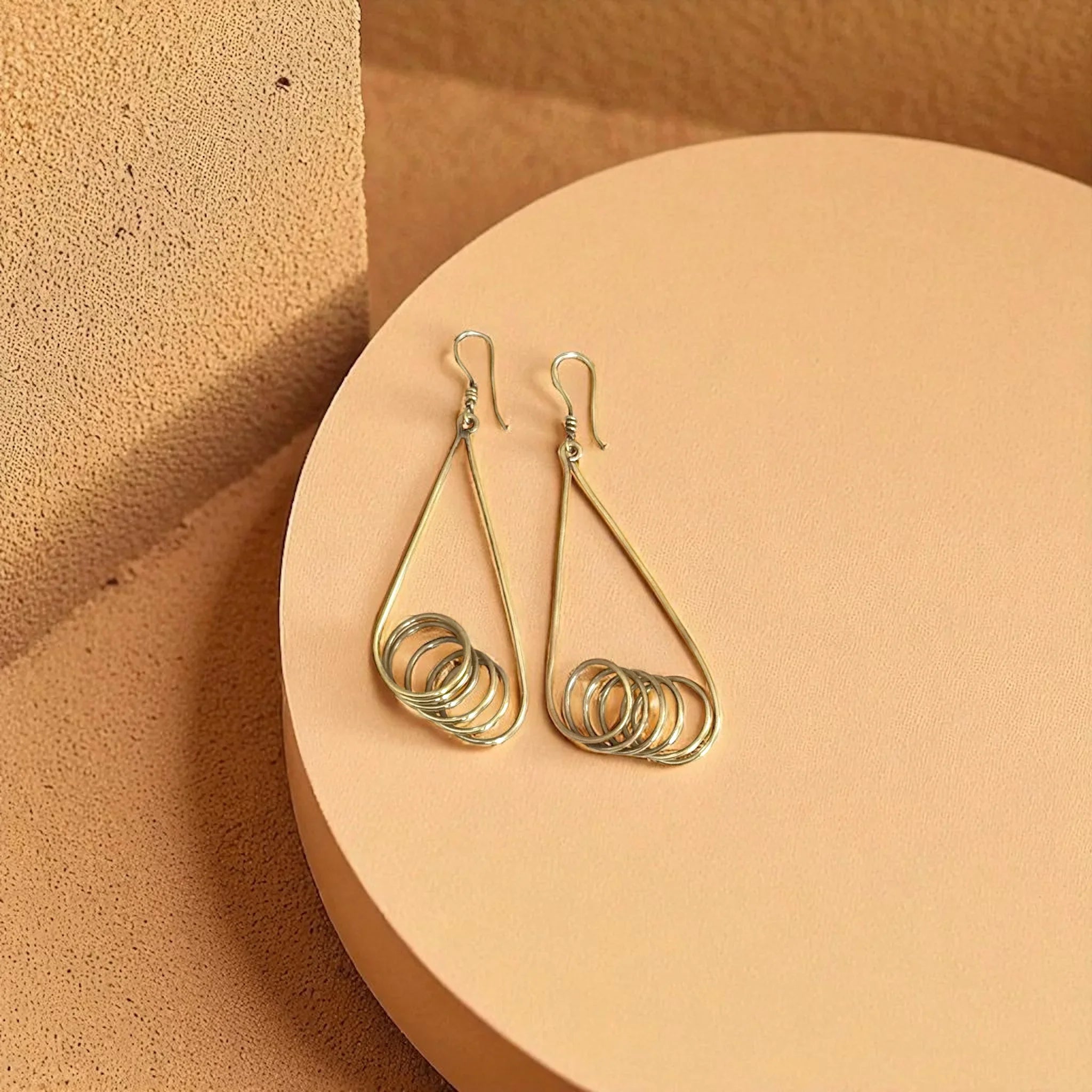 Gold spiral earrings on a round beige platform with a warm brown background