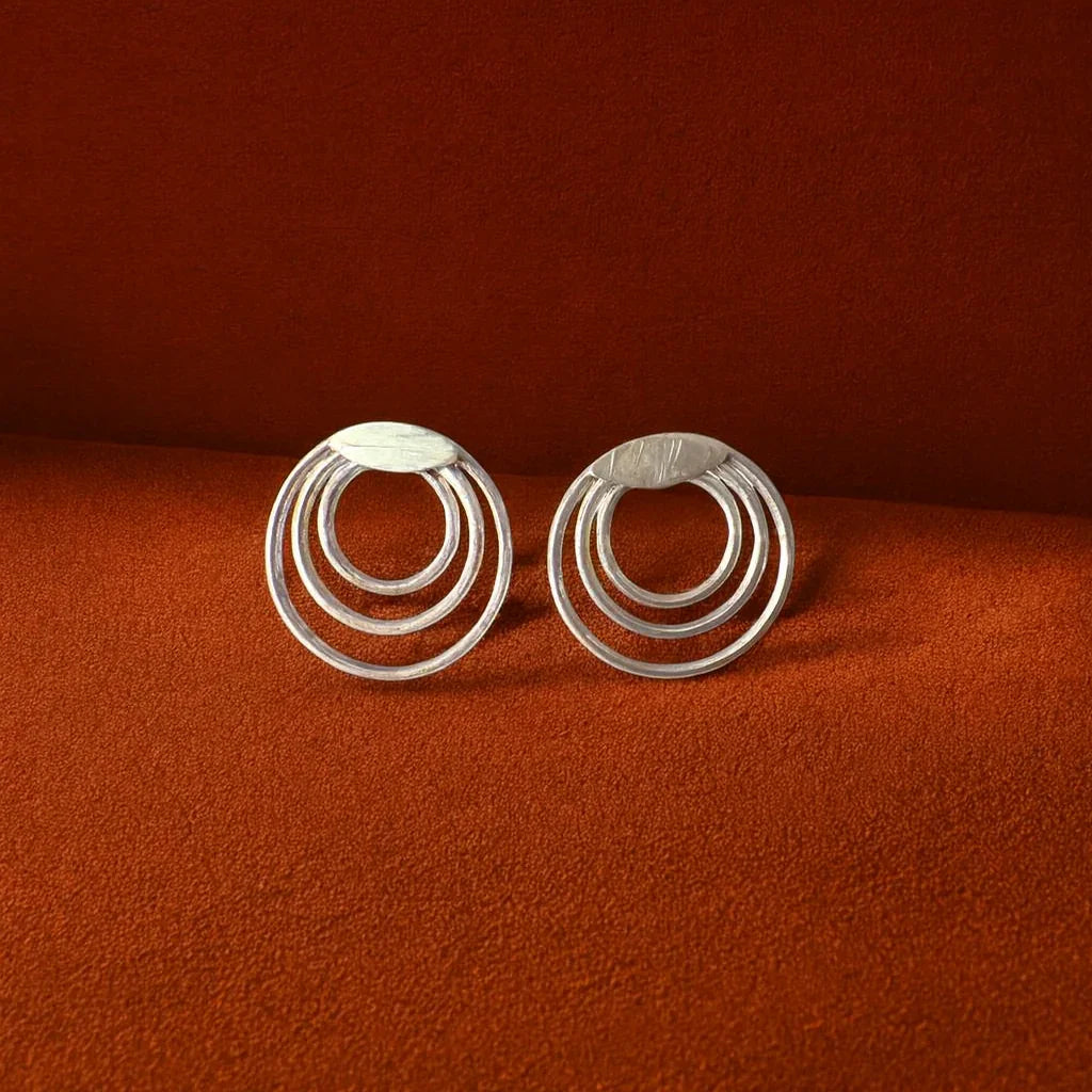 Silver circular earrings on a rust-colored background
