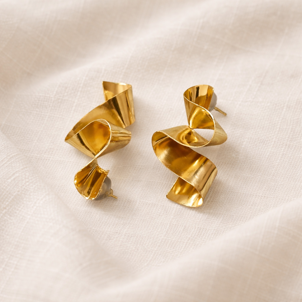 Pair of gold spiral earrings on a beige fabric background