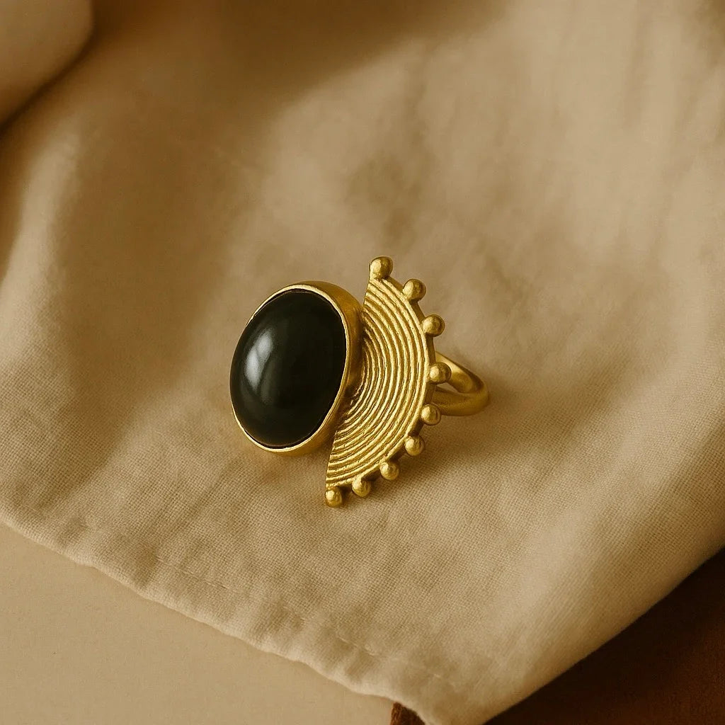 Gold ring with a black gemstone on a beige fabric background