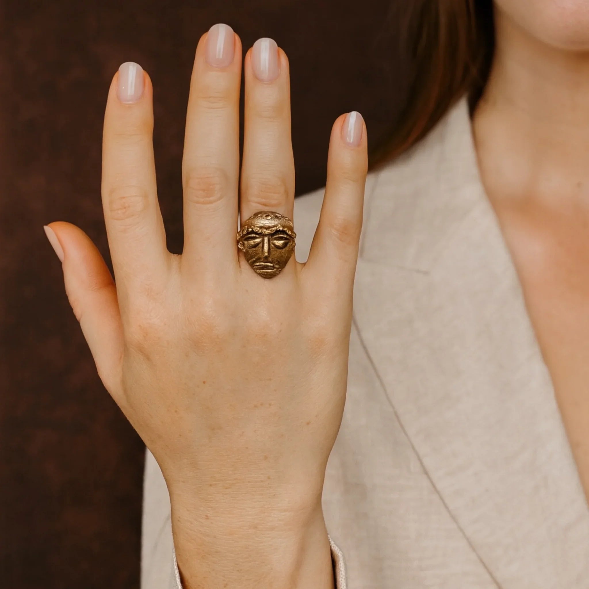 Hand wearing a gold ring with a face design, blurred background