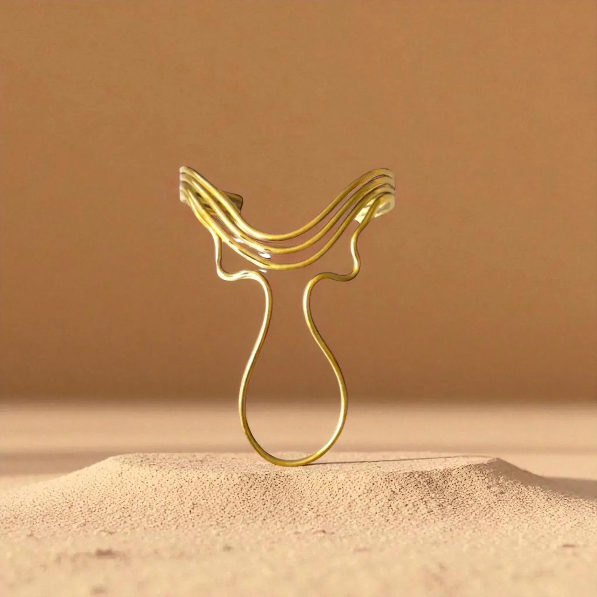 Gold decorative item resembling a horse head on a sand-like surface with a brown background