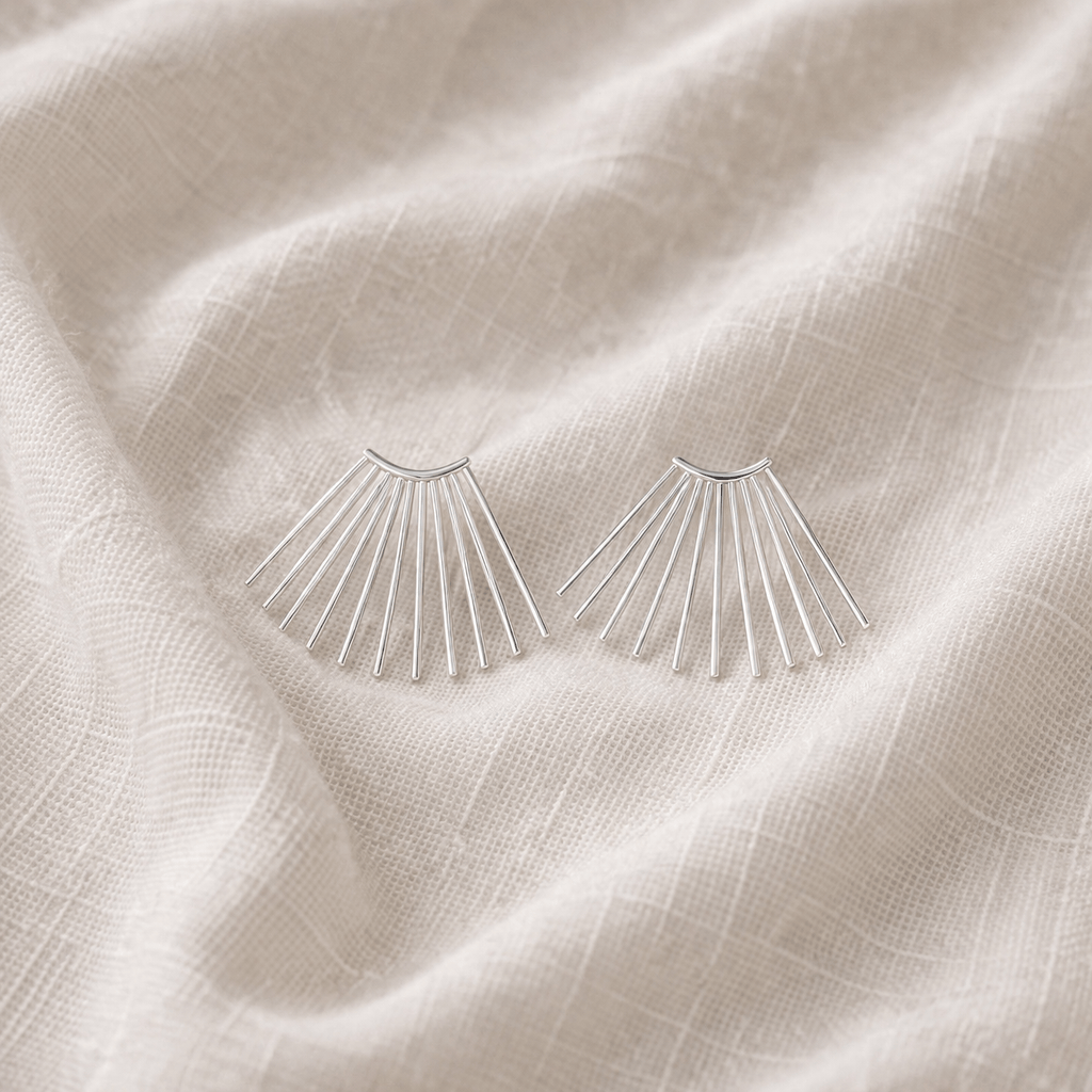 Silver fan-shaped earrings on a textured beige fabric background