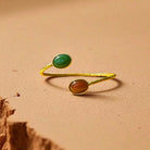 Gold ring with two colored stones on a sandy surface