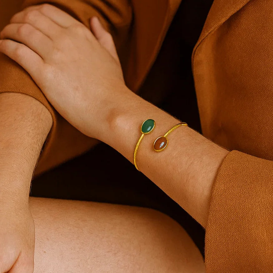 Close-up of a person wearing a gold bracelet with green gemstones, holding another person's hand.
