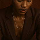 Person wearing a brown blazer and gold necklace against a brown background