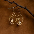 Gold earrings with shell pendants hanging from a branch on a brown background