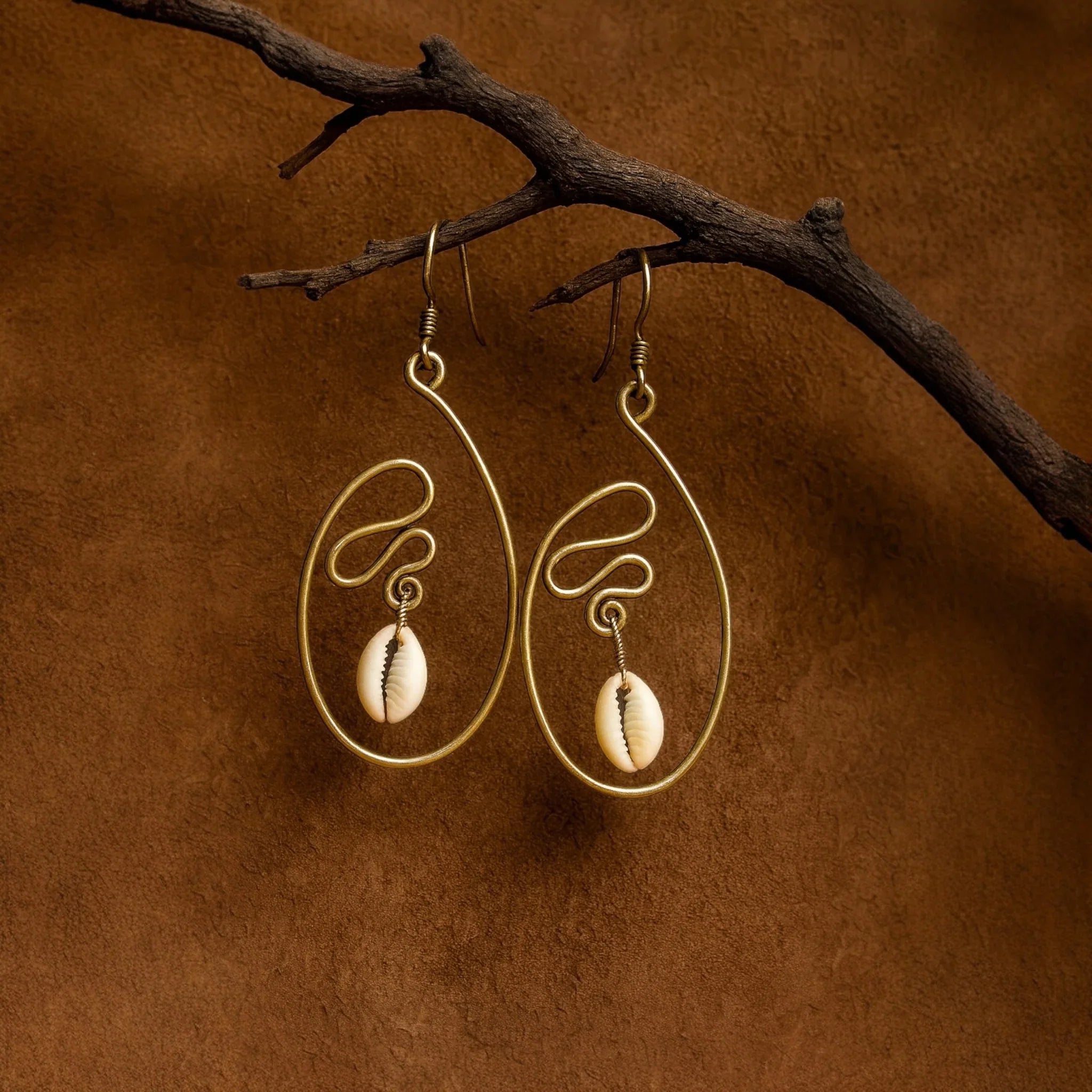 Gold earrings with shell pendants hanging from a branch on a brown background