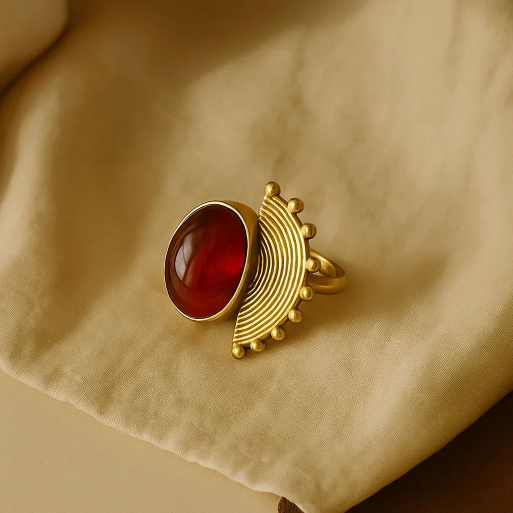 Gold ring with a red stone on a beige fabric background