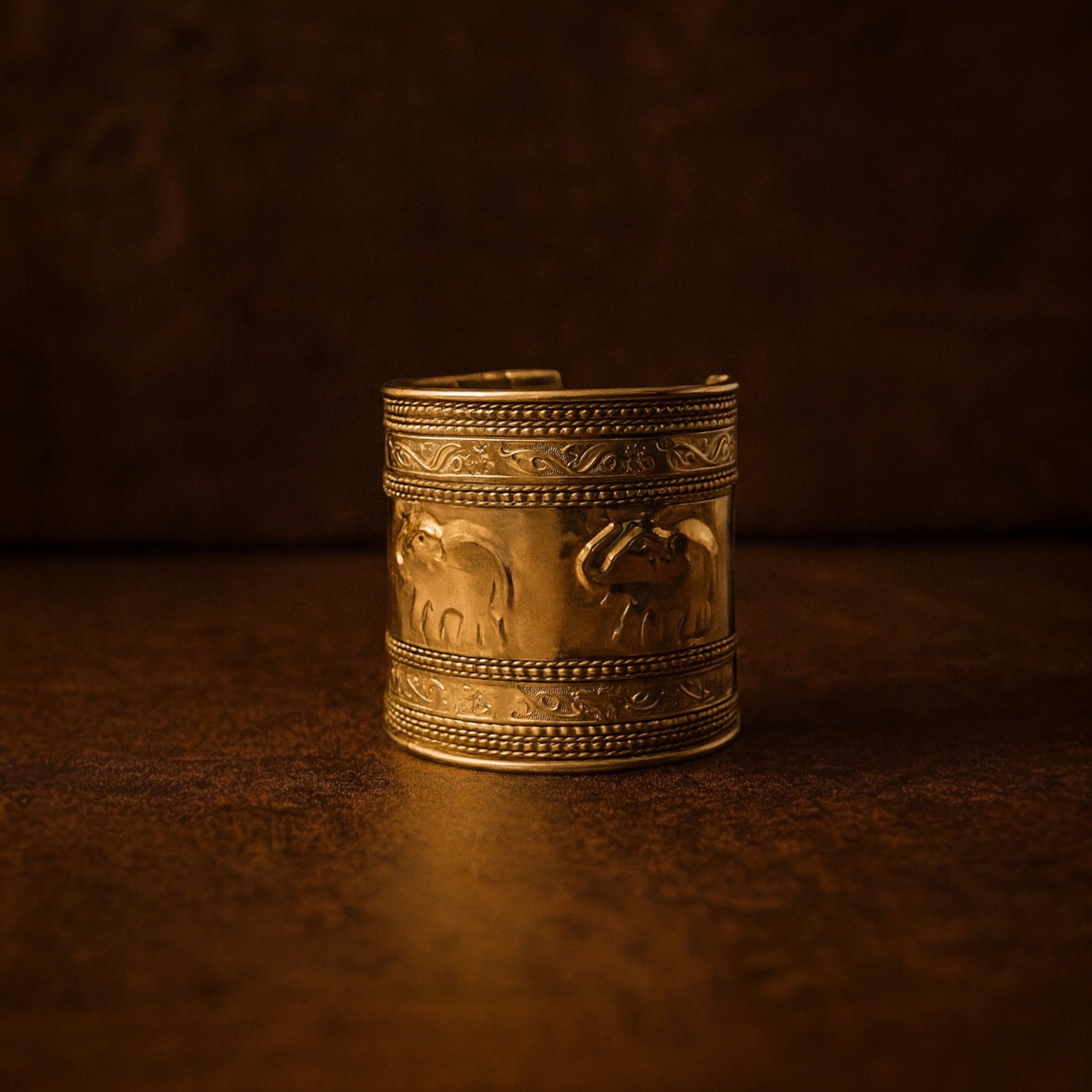 Decorative gold arm cuff with elephant designs on a dark brown background