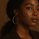 Woman wearing gold hoop earrings against a brown background