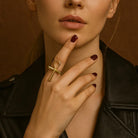 Close-up of a person wearing a gold ring with a cross design on a neutral background