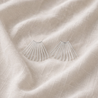 Silver fan-shaped earrings on a textured beige fabric background