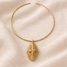 Gold necklace with a face-shaped pendant on a beige fabric background