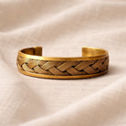 Gold bracelet with braided design on a beige fabric background
